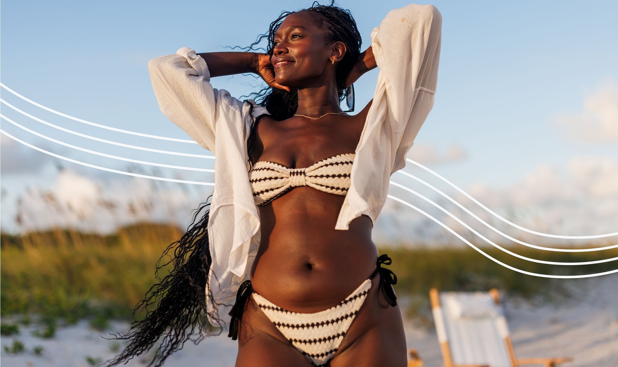 Confident woman in a white and black bikini holding her arms up and smiling with newfound confidence due to her brazilian laser hair removal treatments