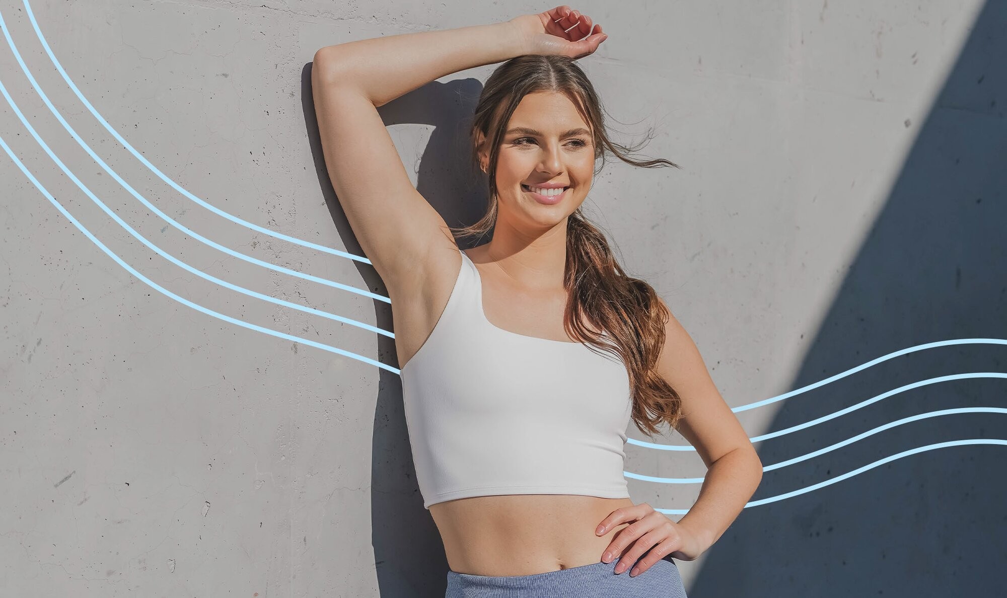 Woman brimming with confidence because she just got arm laser hair removal and is showing off her sleek, hairless arms in a white crop top workout shirt