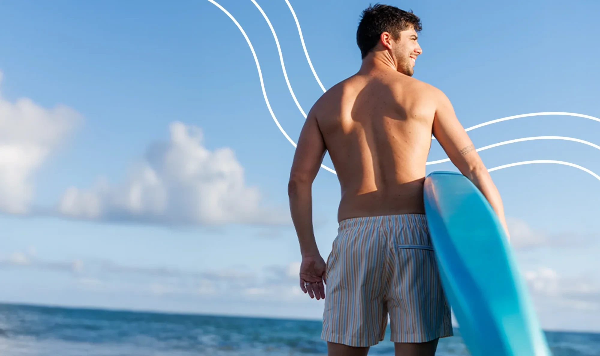 Tanned man with a surfboard under his arm smiling and looking right in front of the ocean