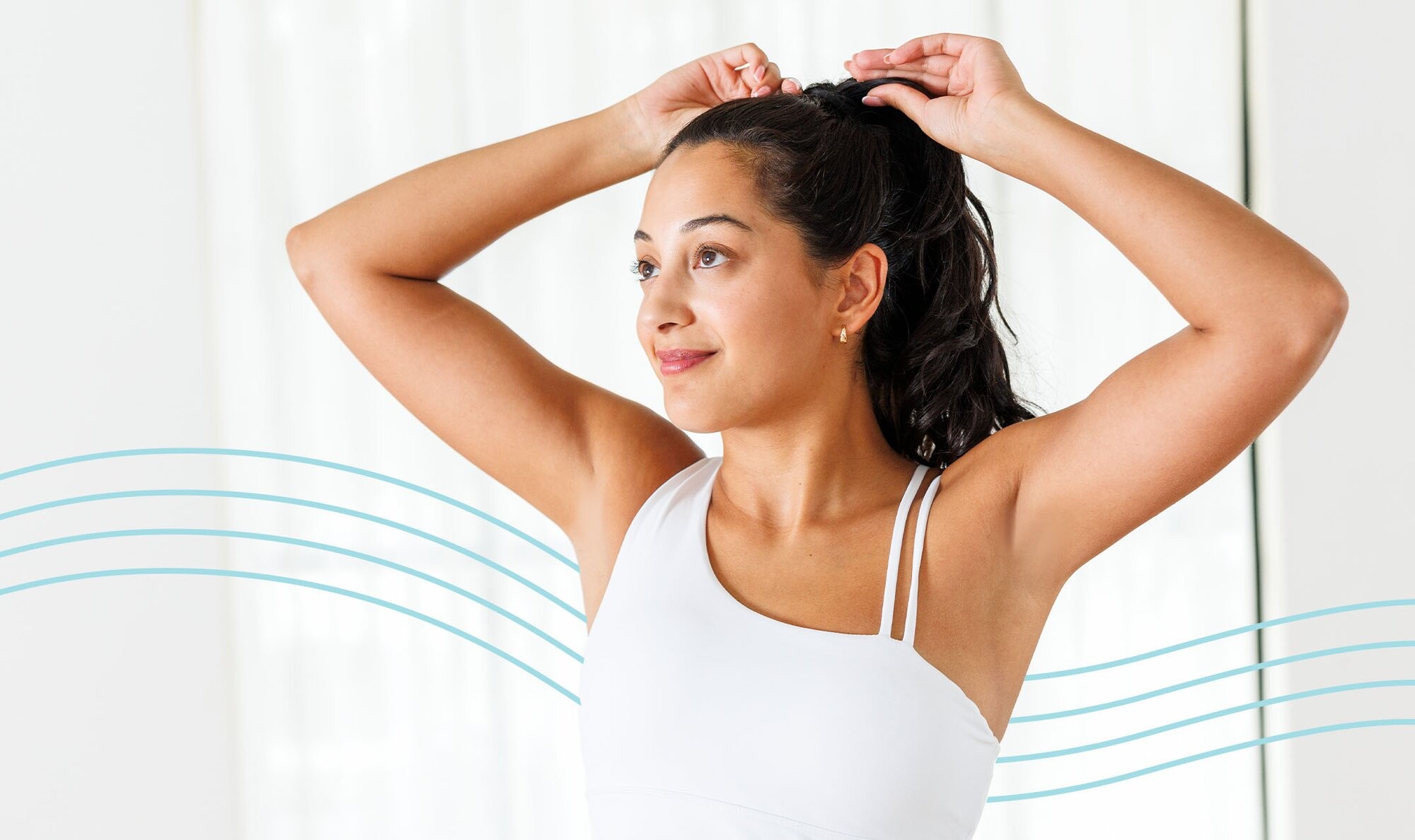 Woman holding her arms above her head and smiling because she's admiring her underarm laser hair removal results while wearing a white off-the-shoulder camisole